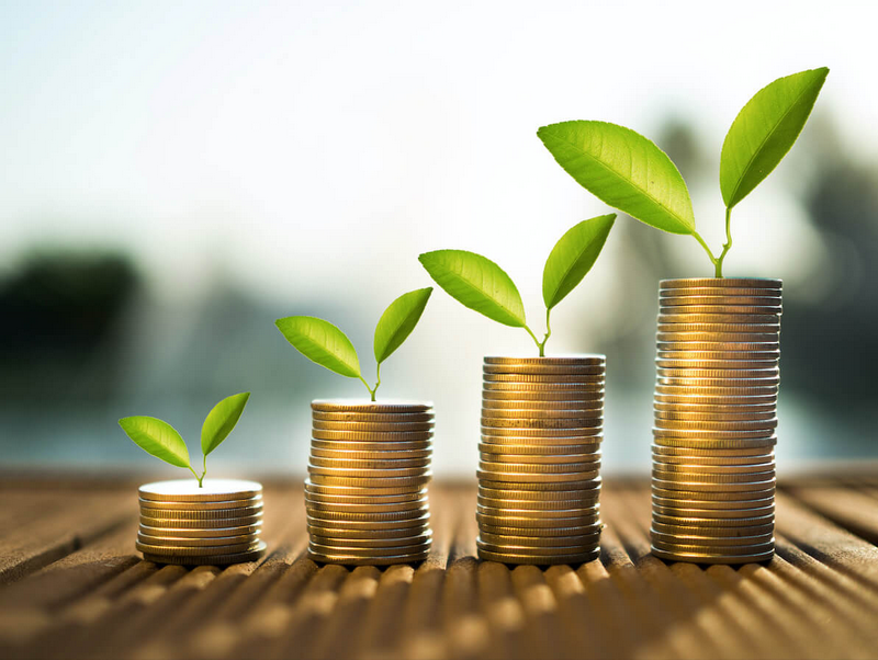 Four stacks of coins on a wooden surface, each with a green leaf growing from the top, symbolizing financial growth and investment