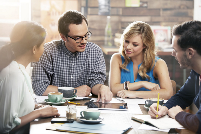 A diverse group of four people collaborating over documents at a coffee shop table.