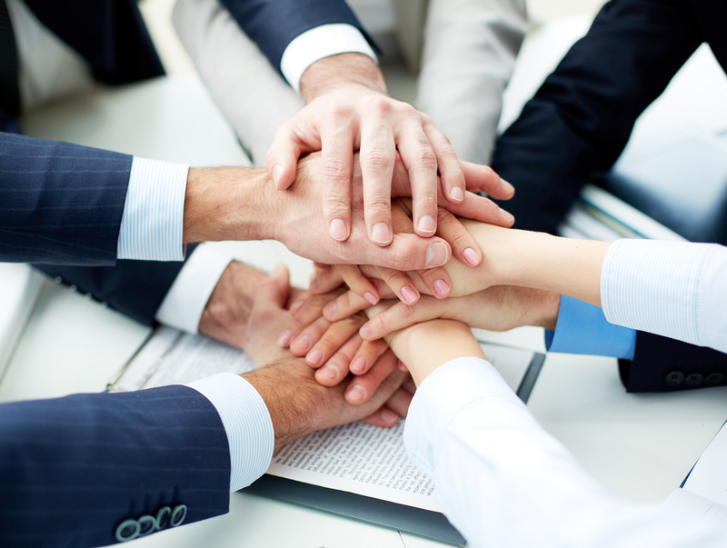 A team of professionals in a meeting stacking hands together over a table as a gesture of unity and teamwork.